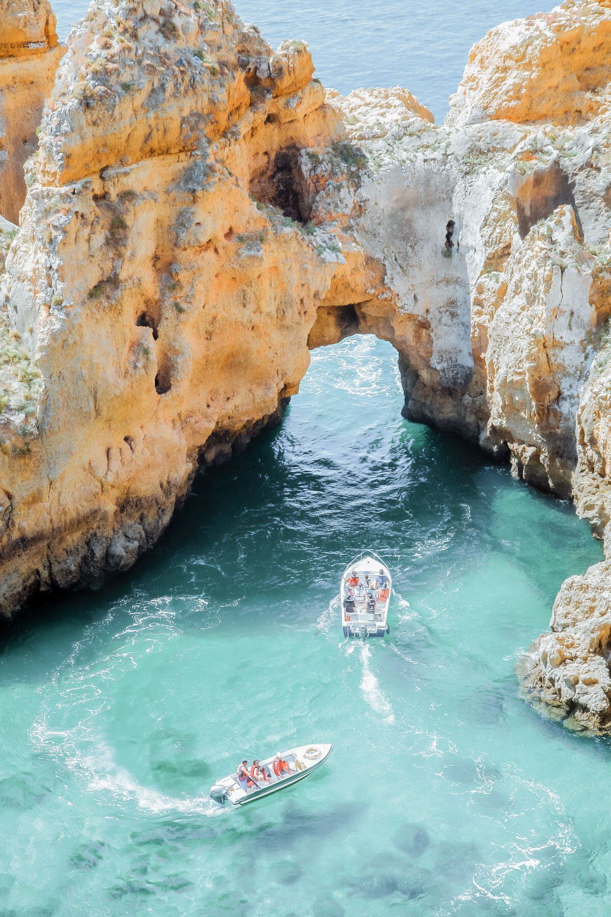 Turquoise cove with rocky arch and three small boats floating in clear water