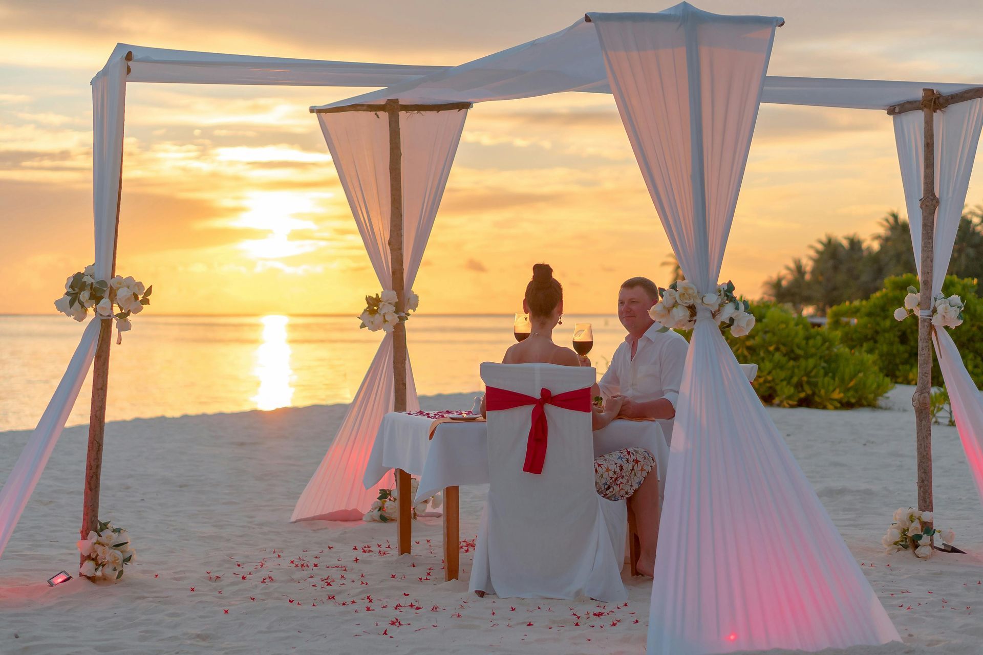 Beach wedding ceremony at sunset under a white canopy by the water
