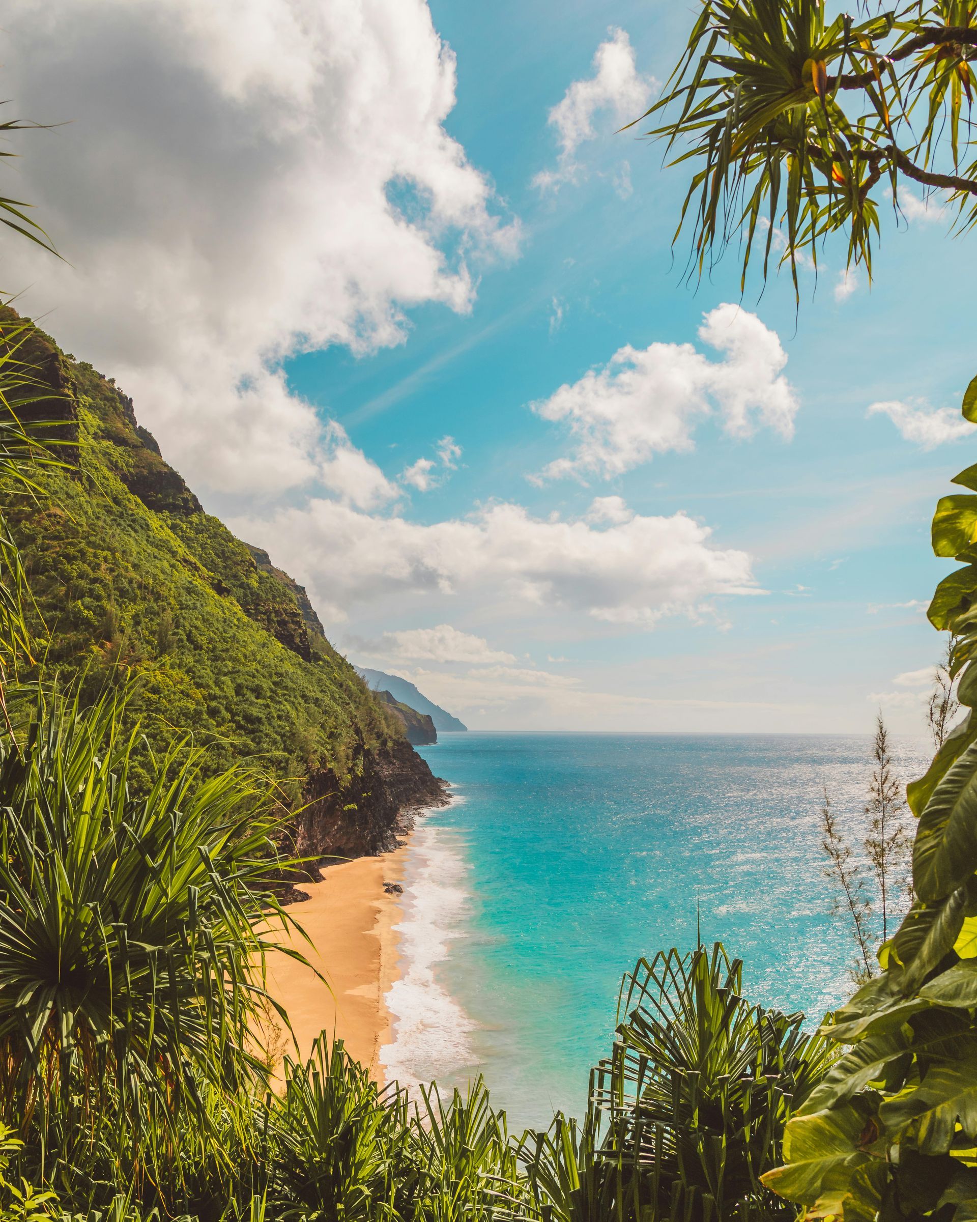 Tropical beach with turquoise water, sandy shore, green cliffs, and a bright blue sky with clouds