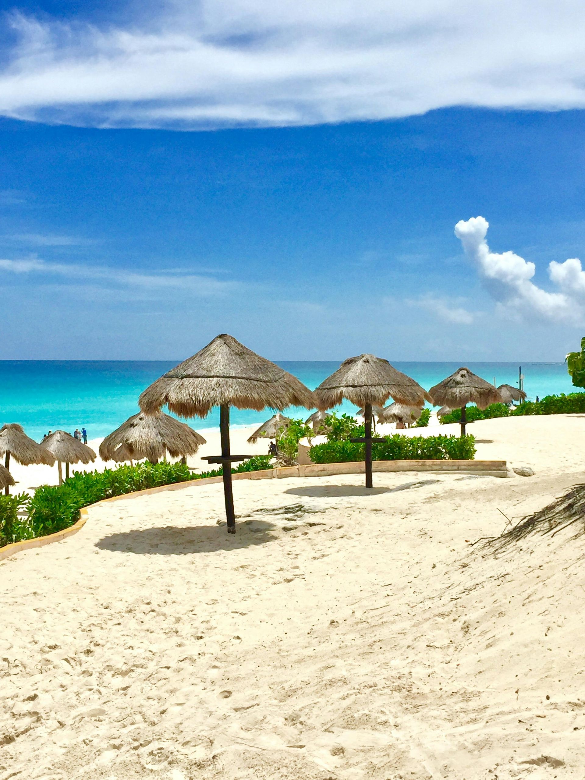 Sandy beach with thatched umbrellas, turquoise water, and a bright blue sky
