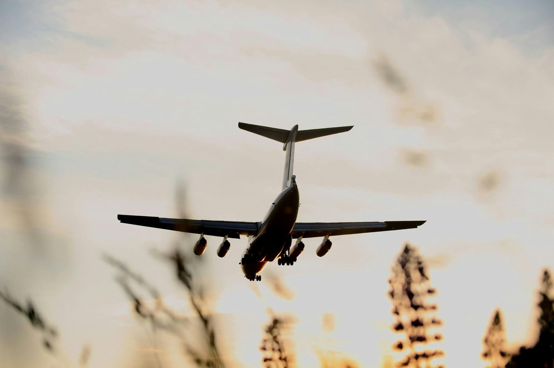 Airplane silhouetted against a cloudy sky, seen from below during landing or takeoff