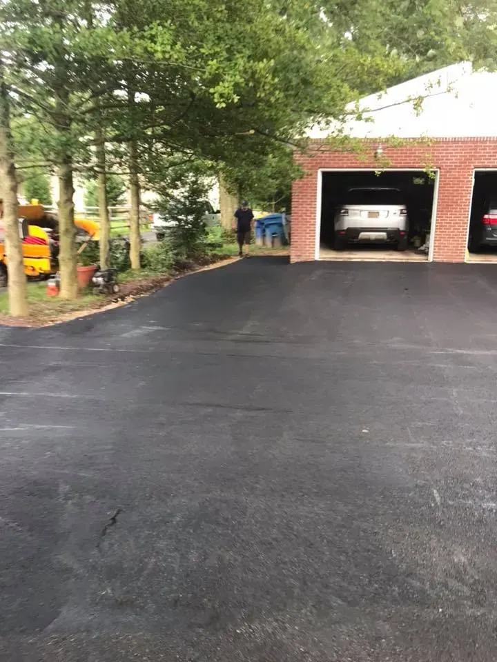 Newly paved asphalt driveway leading to a brick garage with cars parked inside.