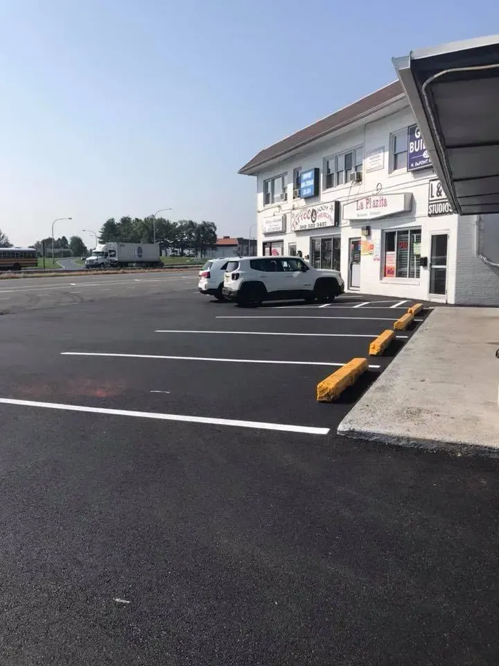 Black asphalt parking lot next to a white building with businesses. A white SUV is parked.