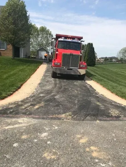 Red dump truck on driveway near a house, preparing to pave.