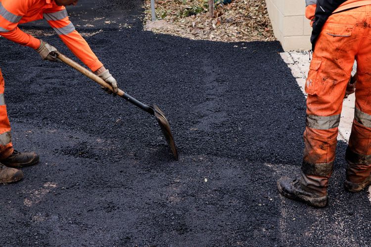 Workers in orange overalls laying asphalt with shovels.