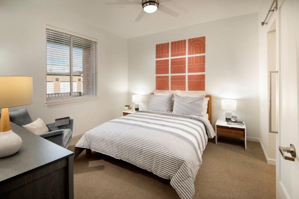 Cozy bedroom with a queen bed, striped bedding, two nightstands, lamps, and orange wall art.