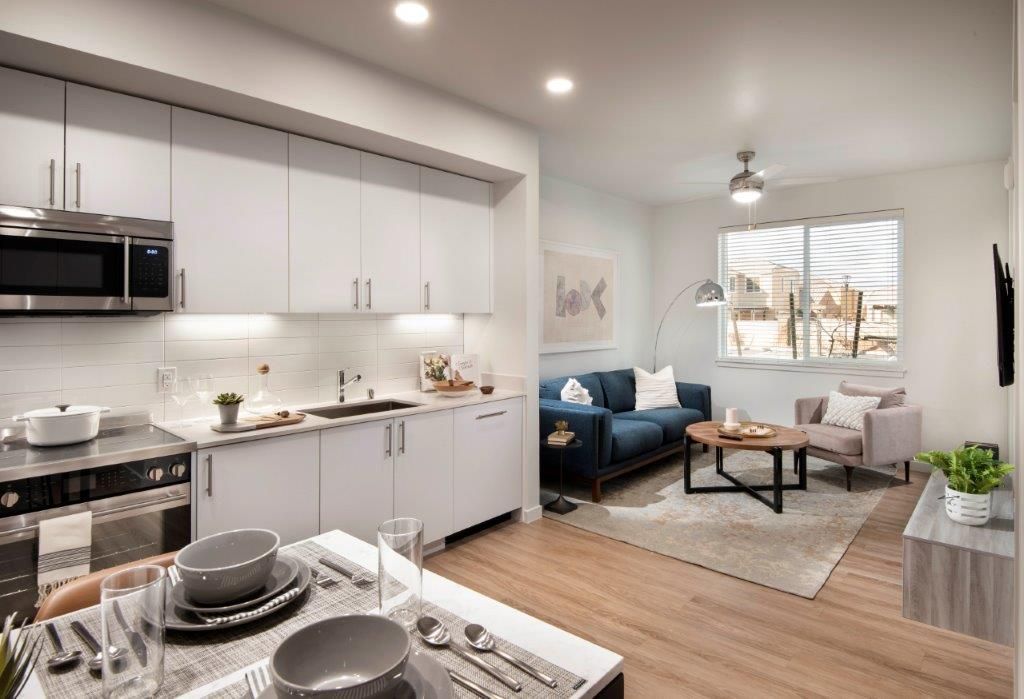 Open-concept kitchen and living area in a modern apartment with white cabinets, stainless appliances, and a blue sofa.