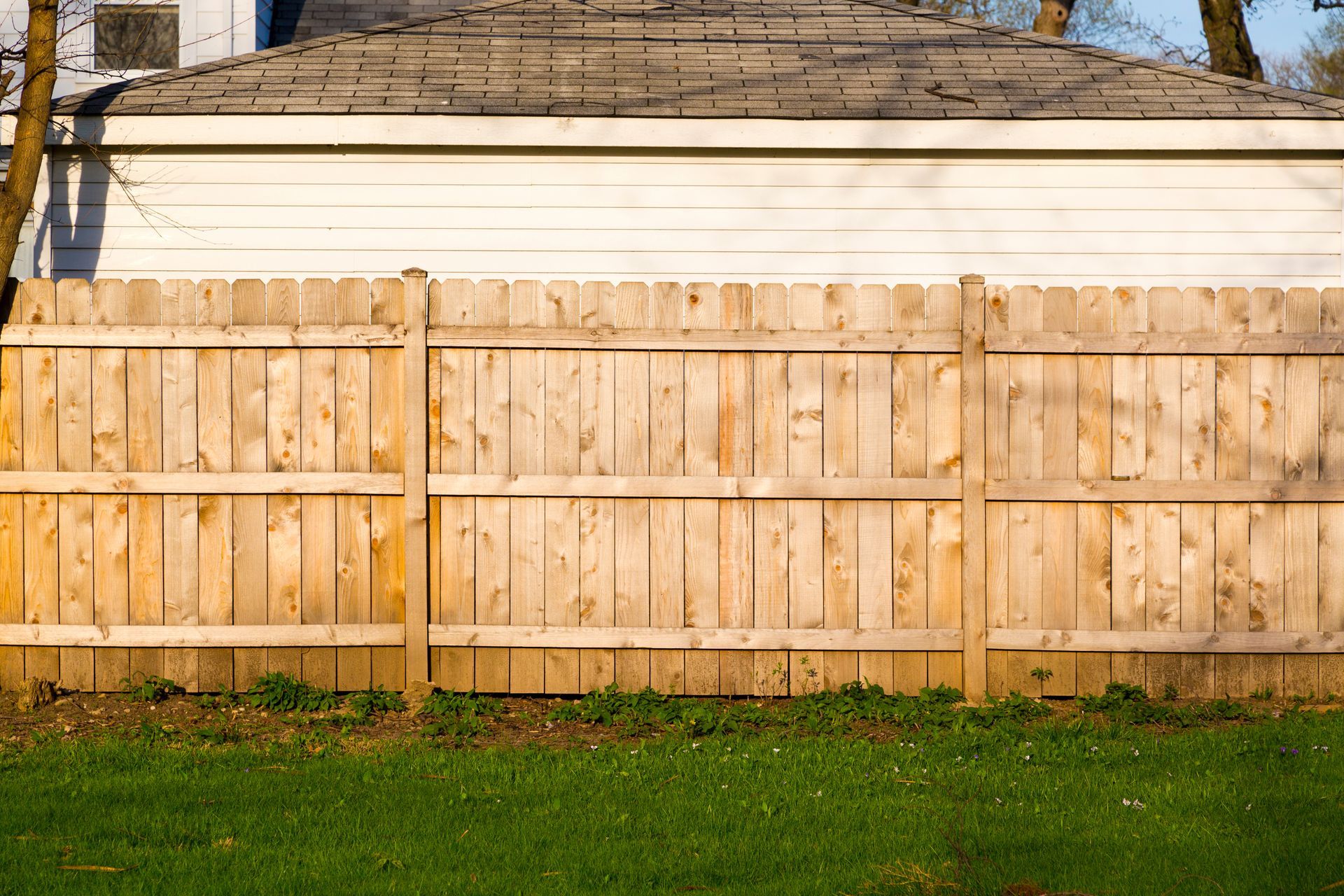 Wooden fence in front of a white building with a brown roof, green grass in the foreground.