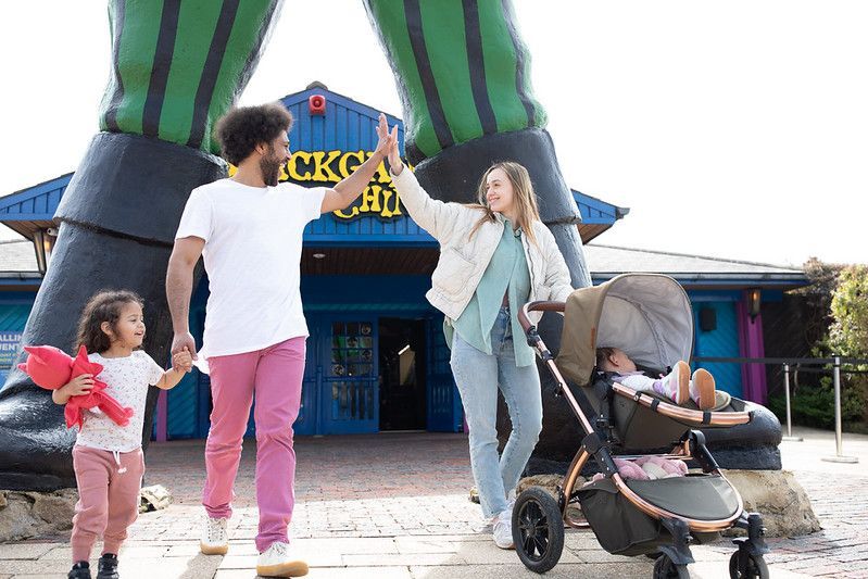 A family high-fives while standing in front of a giant green-legged sculpture outside a blue building.