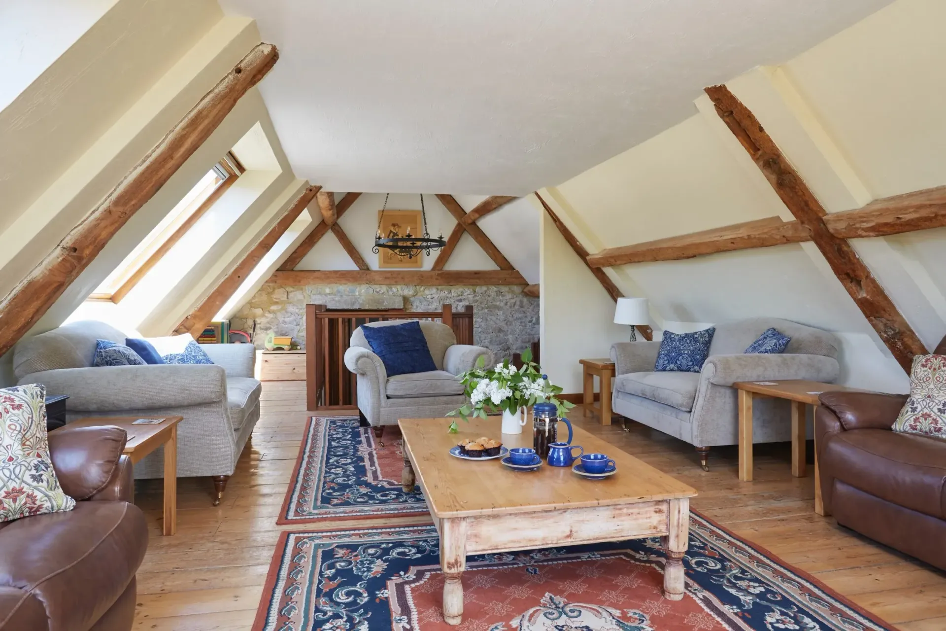 Attic living room with exposed wood beams, skylights, multiple sofas, a central coffee table, and patterned area rugs.