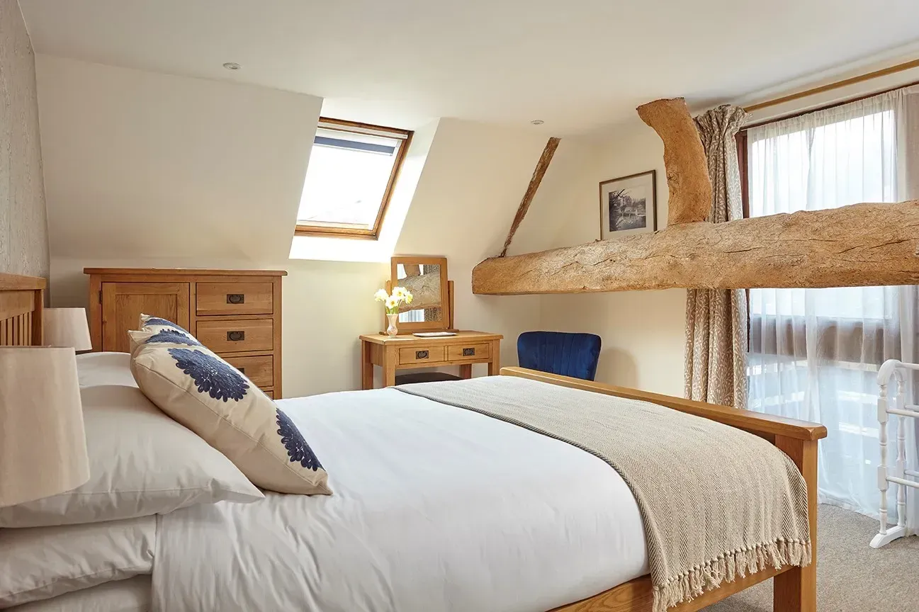 A cozy bedroom with a wooden bed, a large overhead exposed beam, a skylight, and a small vanity table in an attic room.