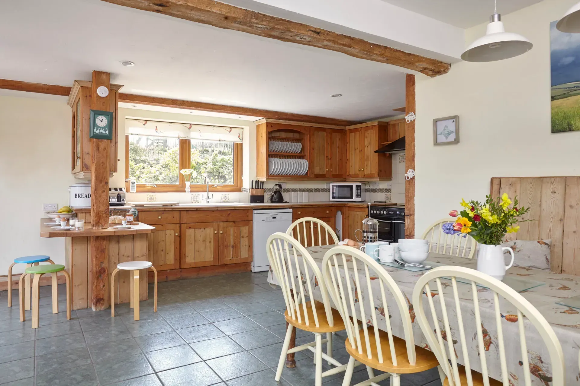A rustic kitchen and dining area with wooden cabinetry, a tiled floor, and a dining table set with flowers.