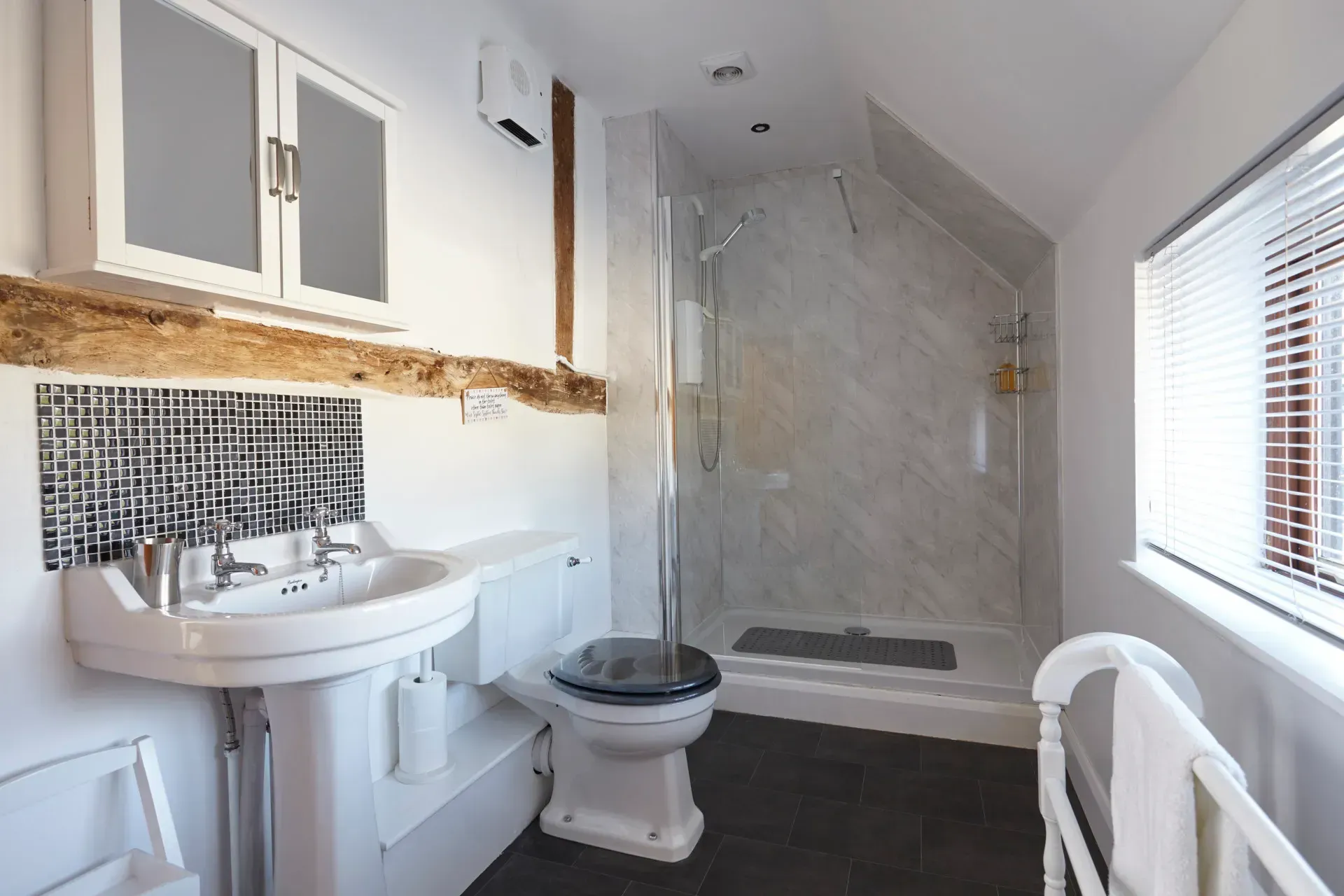 A bright bathroom features a pedestal sink, toilet, glass-enclosed shower, and rustic wood-accented walls.
