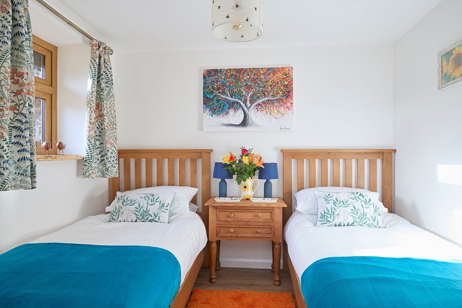 A bedroom with two twin beds featuring white bedding, teal blankets, wooden headboards, and a central nightstand.