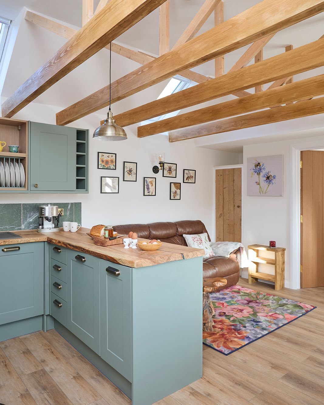Open-plan kitchen and living room featuring blue cabinets, wood countertops, exposed ceiling beams, and a floral rug.