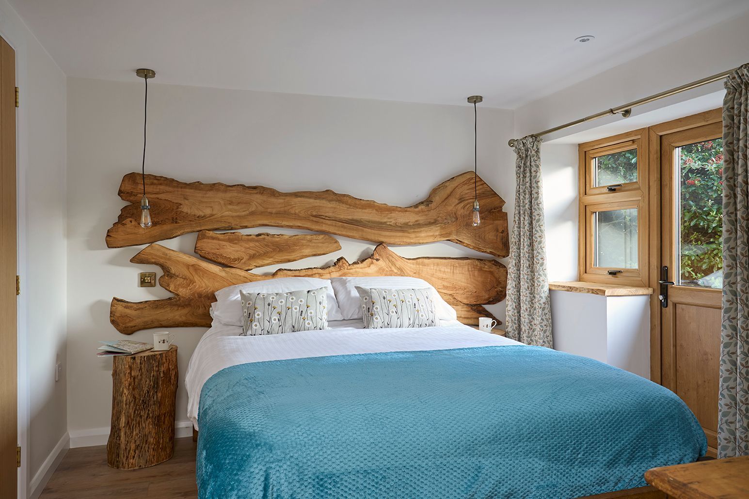 A bedroom with a rustic live-edge wood headboard, a blue textured bedspread, a log side table, and a glass door.