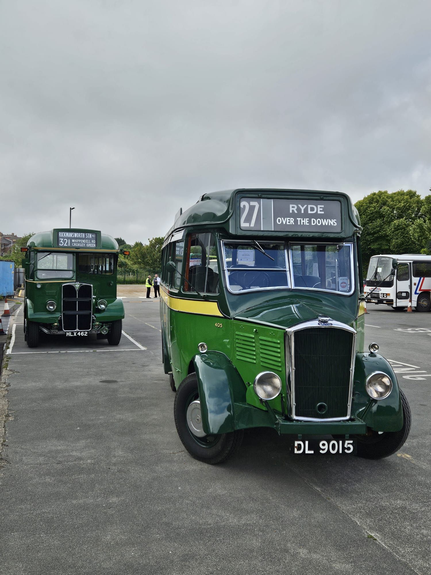 Two green vintage buses parked on a cloudy open lot, one facing forward with route 21 displayed.