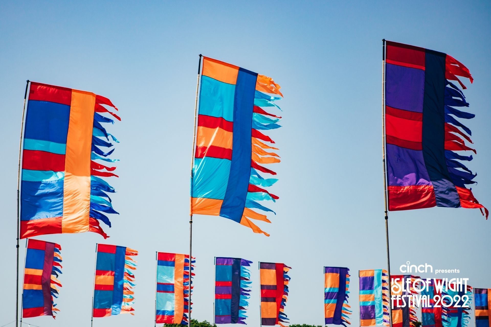 Multicolor shredded flags wave against a clear blue sky at the Isle of Wight Festival 2022.