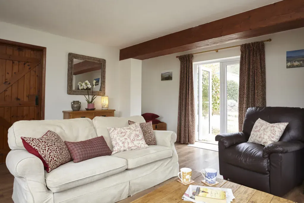 A living room with a white sofa featuring patterned pillows, a brown leather armchair, and a wooden coffee table.