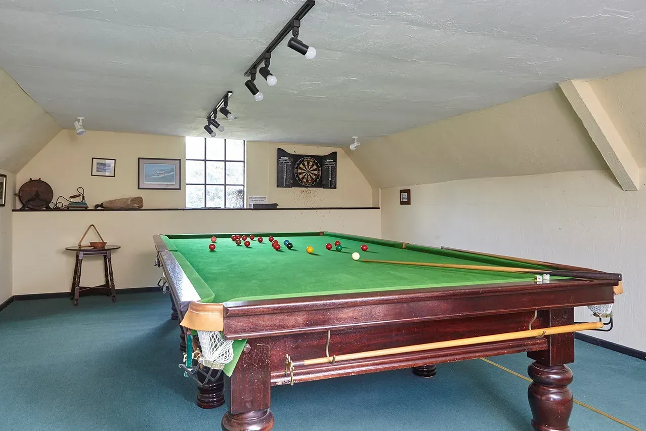 A green-felt snooker table sits in an attic room with cream walls, sloped ceilings, and track lighting.