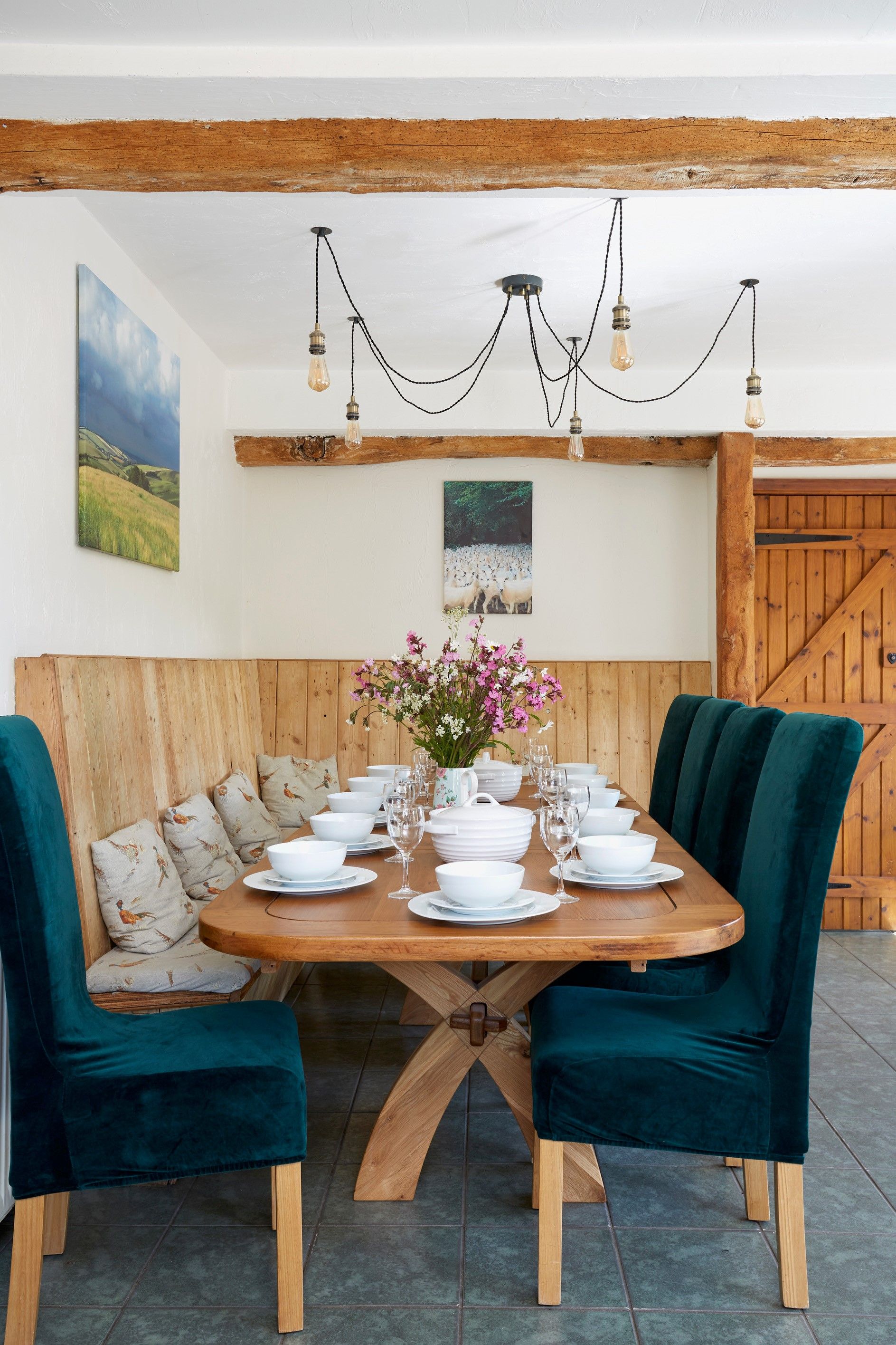 A rustic dining area with wooden cabinetry, a tiled floor, and a dining table for 12 set with flowers.