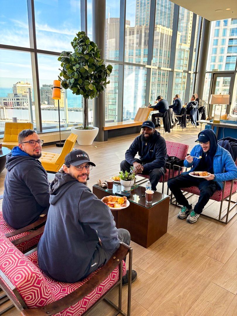 People seated around a table in a bright lounge with large windows and city views