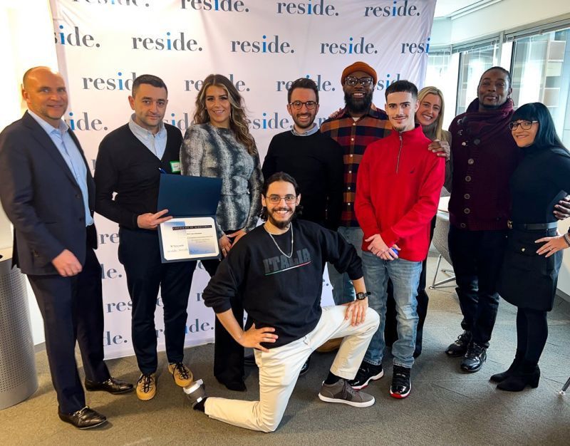 Group of people posing indoors at a RESIDE event, with one holding a framed certificate.