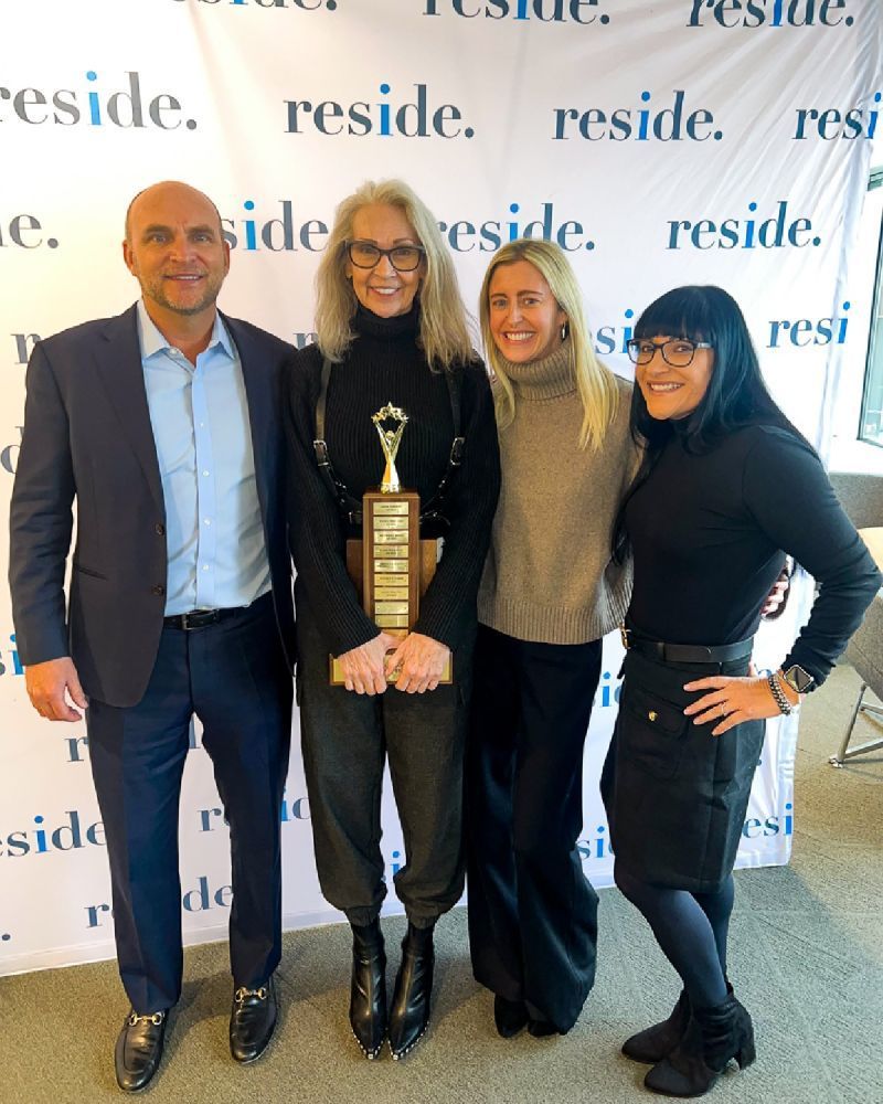 Four people posing with an award trophy in front of a “reside” backdrop at an event.