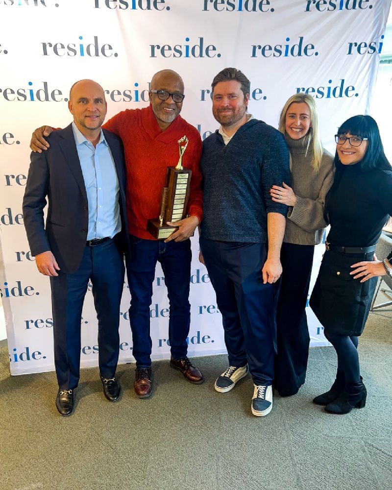 Five people posing at an award event, with one person holding a trophy in front of a branded backdrop.