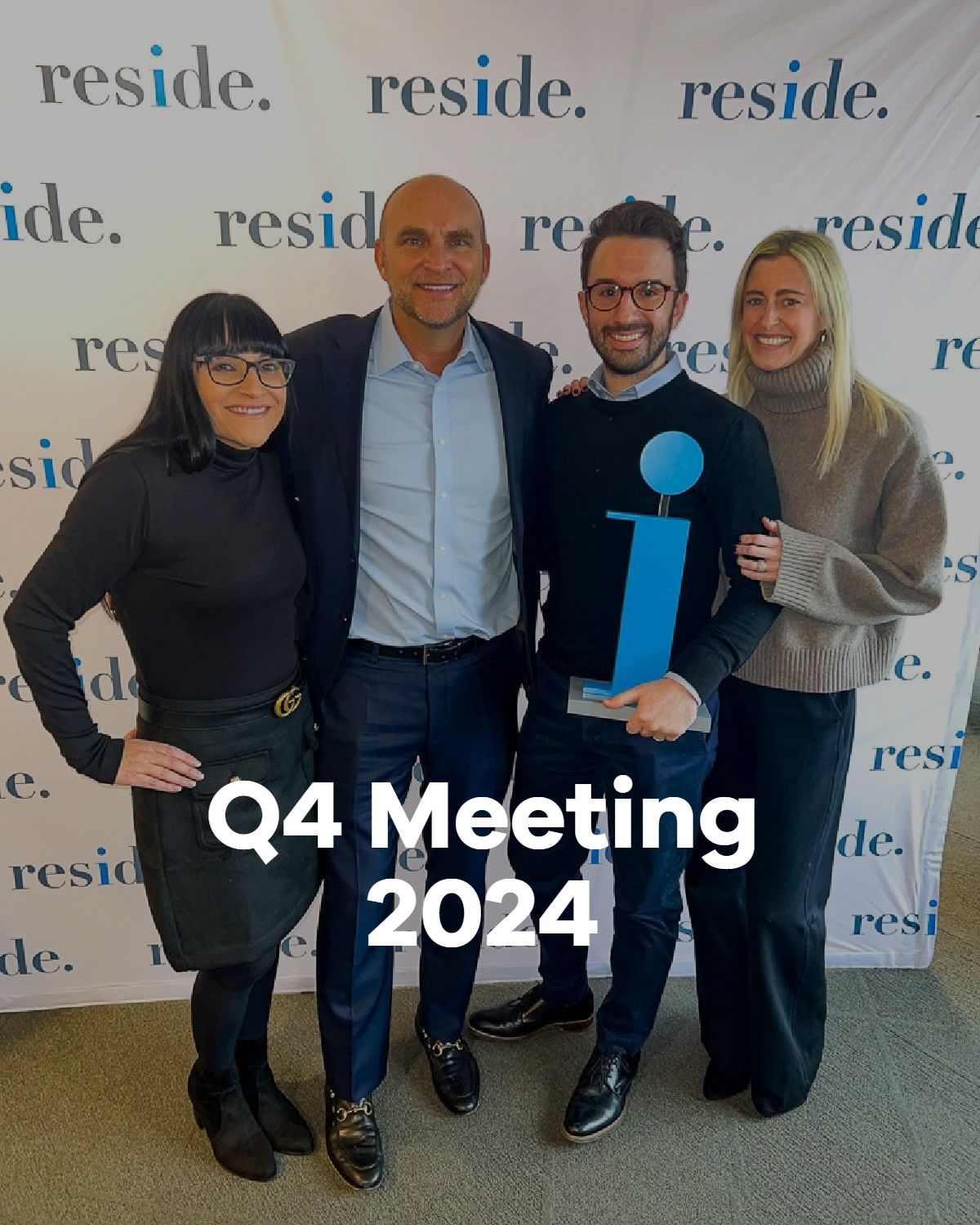Four people posing at a Q4 Meeting 2024 event, holding a blue award sign in front of a branded backdrop