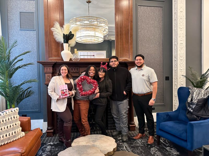 Five people posing in a stylish living room near a fireplace and blue chairs.
