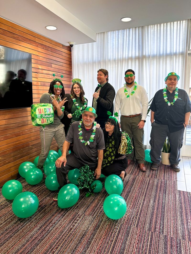 Group posing indoors with green balloons and festive St. Patrick’s Day accessories