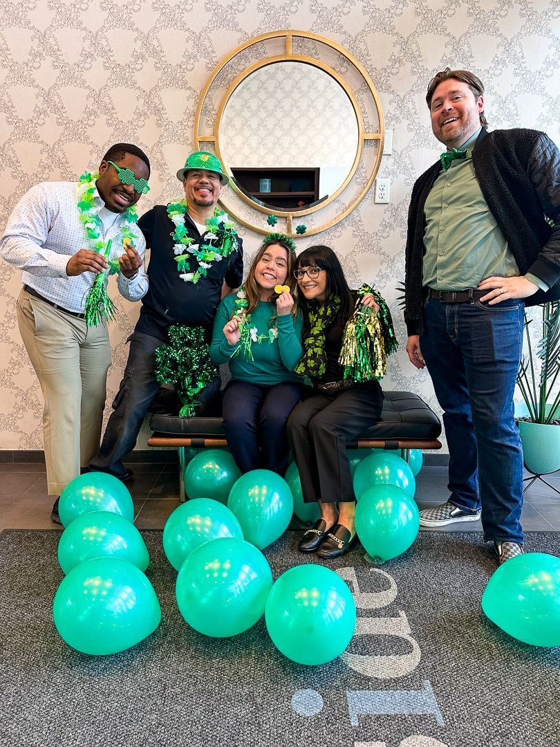Five people posing indoors with green balloons and matching green accessories in a decorated room