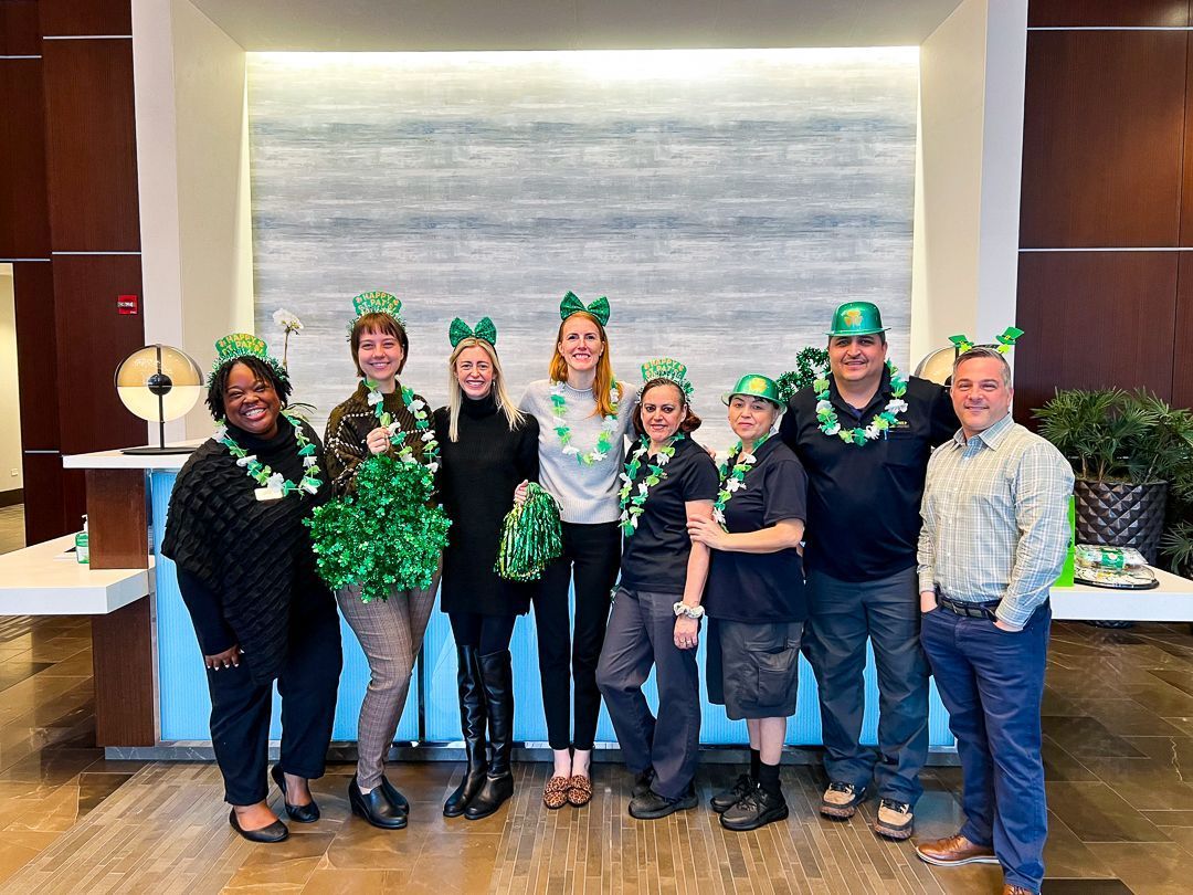 Group posing indoors in green St. Patrick’s Day outfits with shamrock hats and props