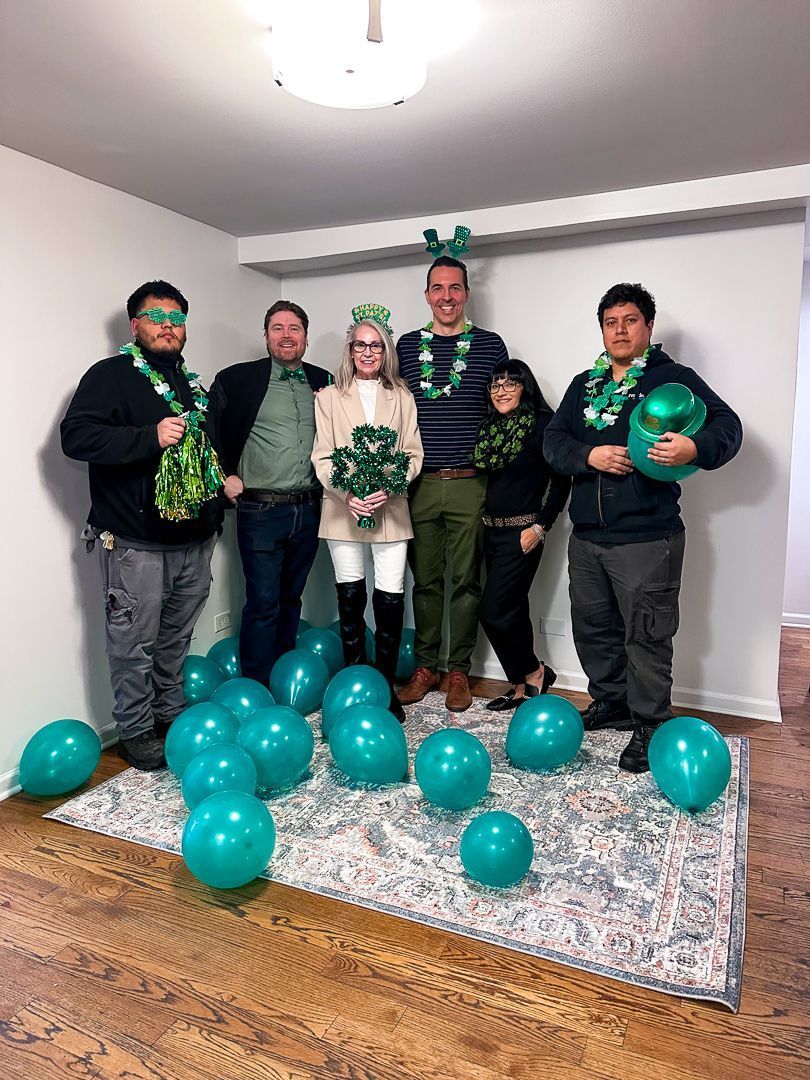 Five people posing indoors with teal balloons and party decorations on a rug