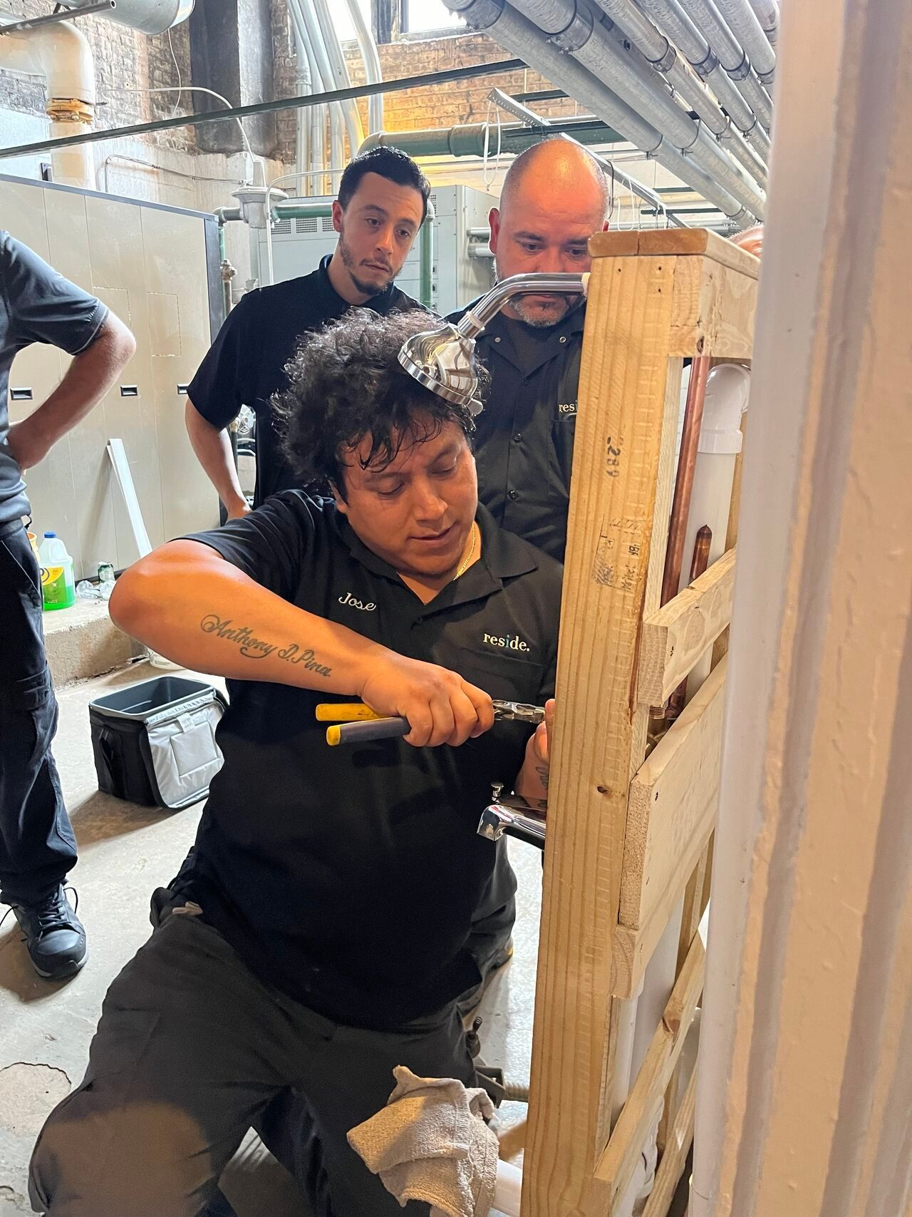 Person using a drill to work on a wooden frame while others watch in a workshop