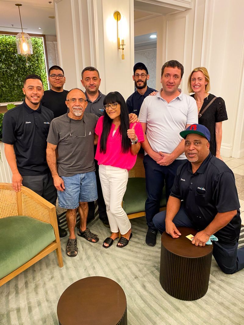 Group of people posing together in a bright living room, with a green chair and round stools in the foreground.