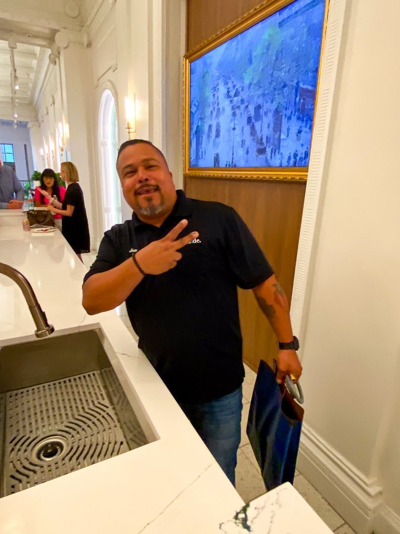 Man posing in a hallway, making a peace sign beside a sink and a large blue wall screen.