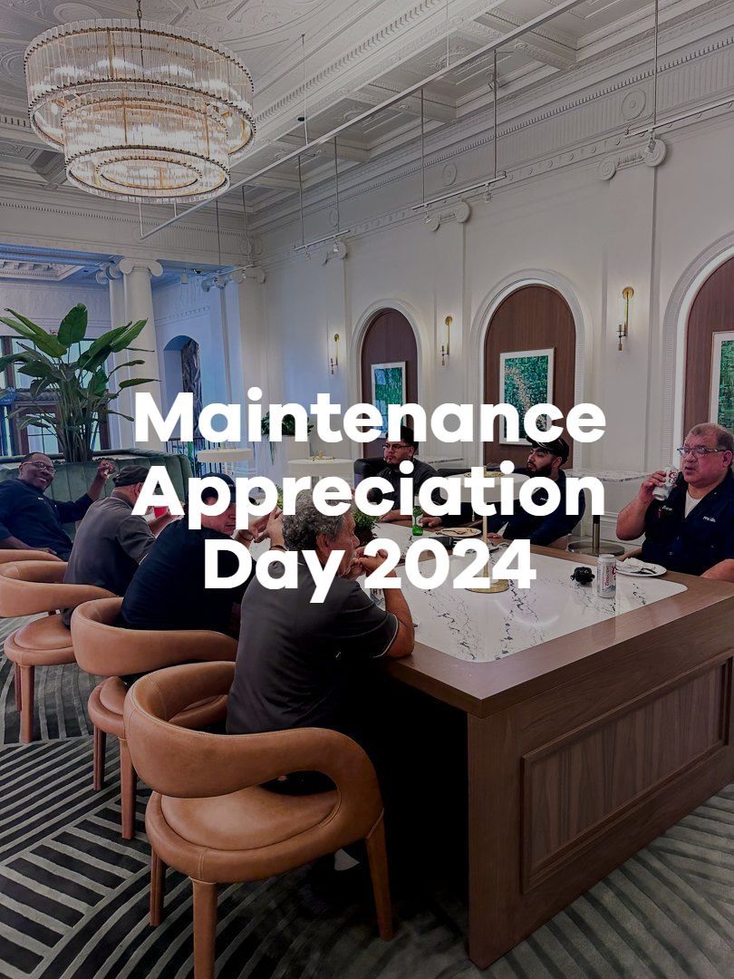People gathered in a hotel lobby for Maintenance Appreciation Day 2024, with a large chandelier and bar seating.