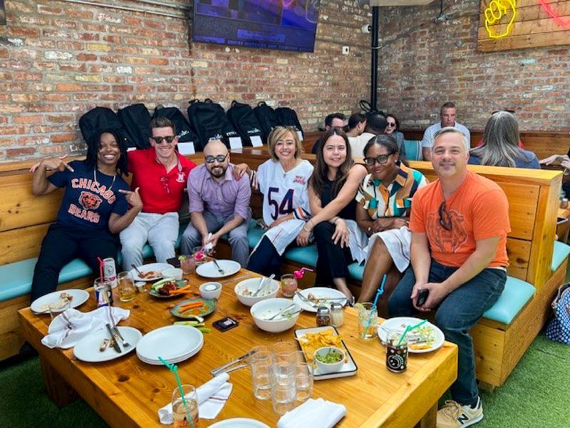 Group of people smiling on colorful couches around a restaurant table with plates and drinks
