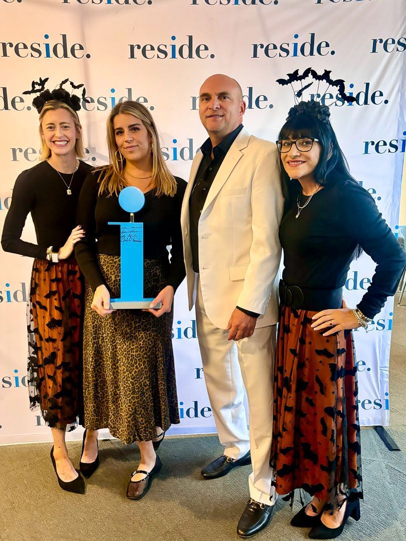 Four people posing at a reception; one holds a blue award plaque in front of a branded backdrop.