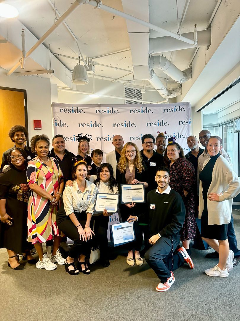 Group of people posing indoors with certificates in a bright event space with a branded backdrop