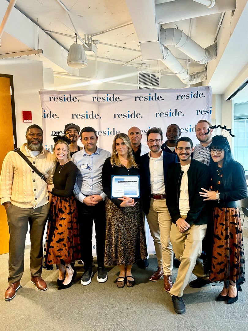 Group posing at a branded event, holding a tablet in a bright office space.