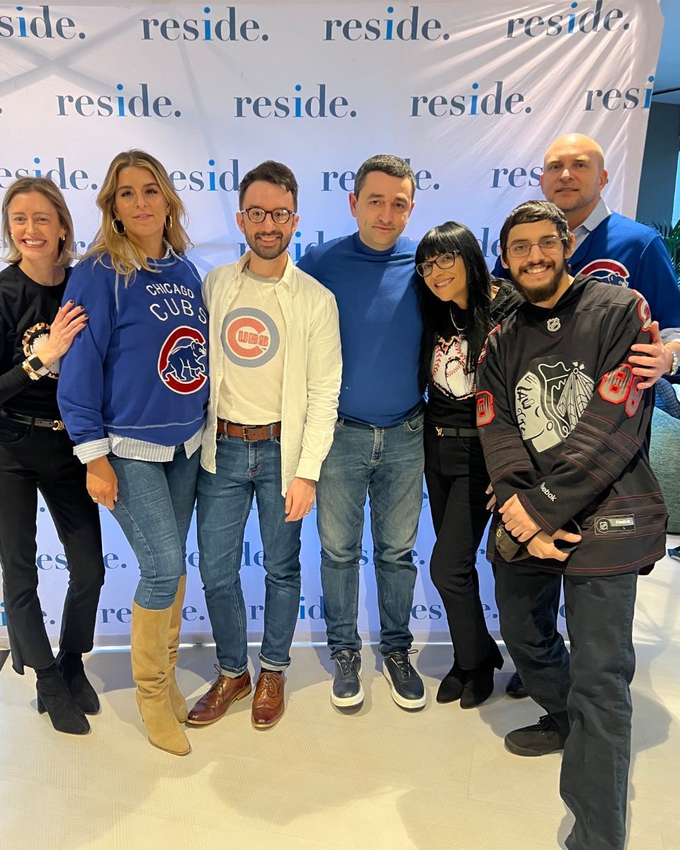 Six people posing together in front of a branded backdrop at an indoor event.
