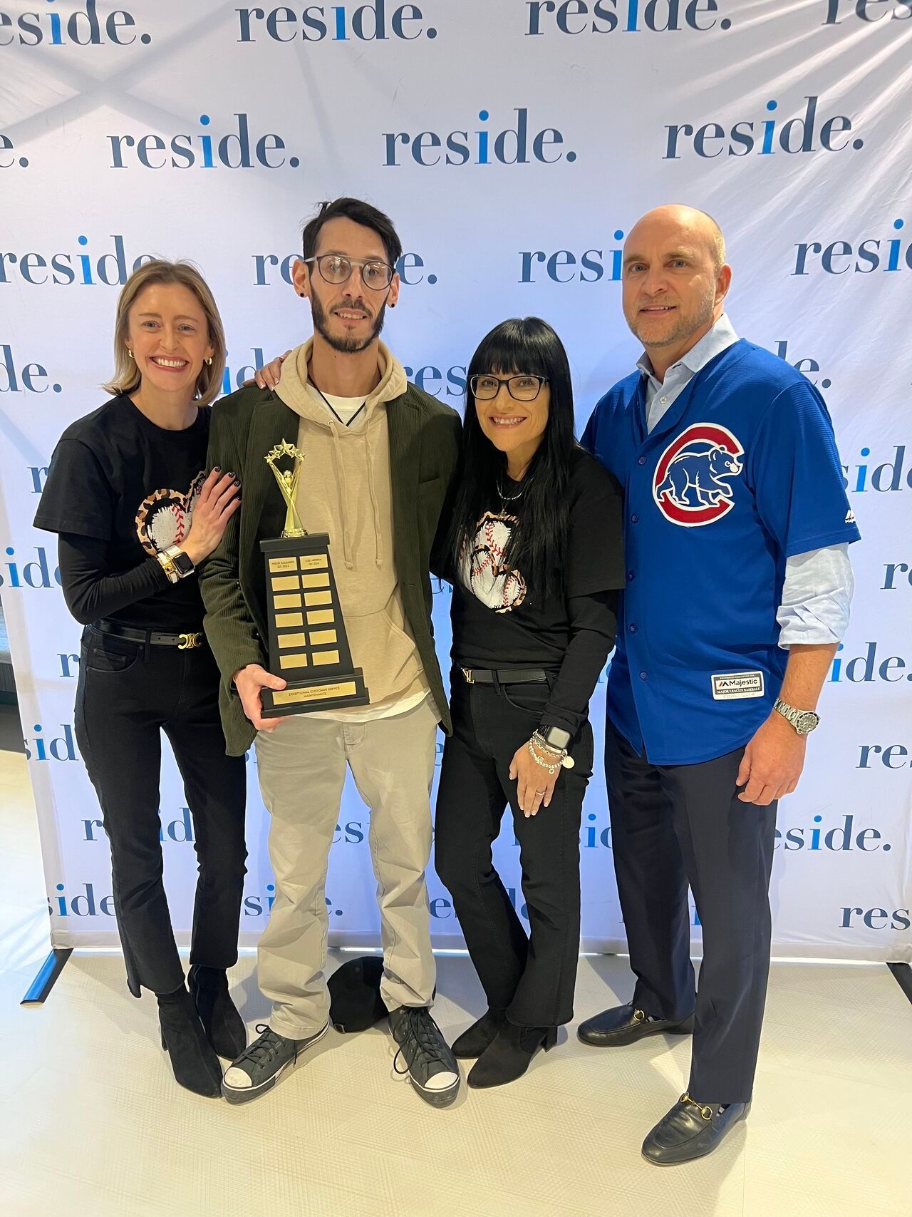 Four people pose at an event backdrop, one holding a gold plaque, with “reside” repeated behind them.