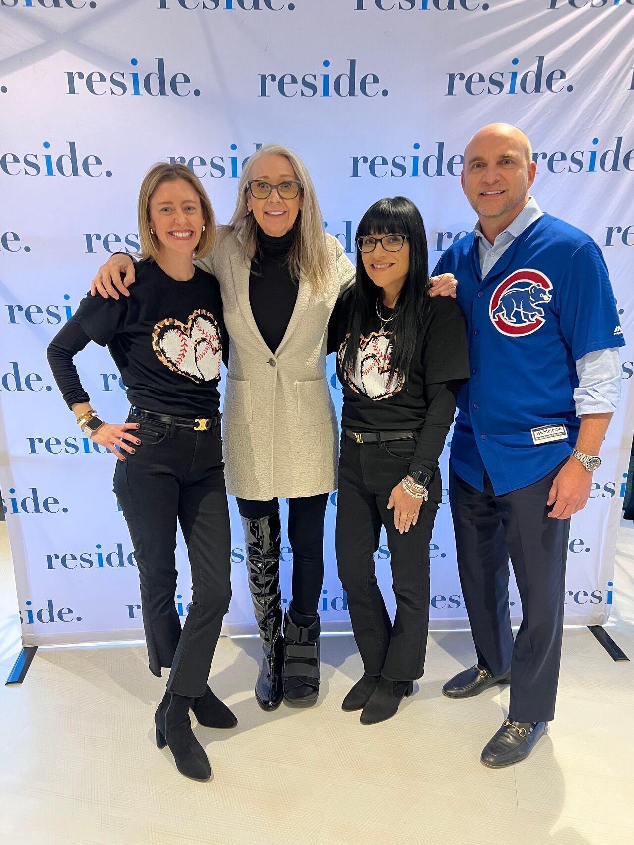 Four people posing indoors in front of a branded backdrop, smiling with arms around each other.