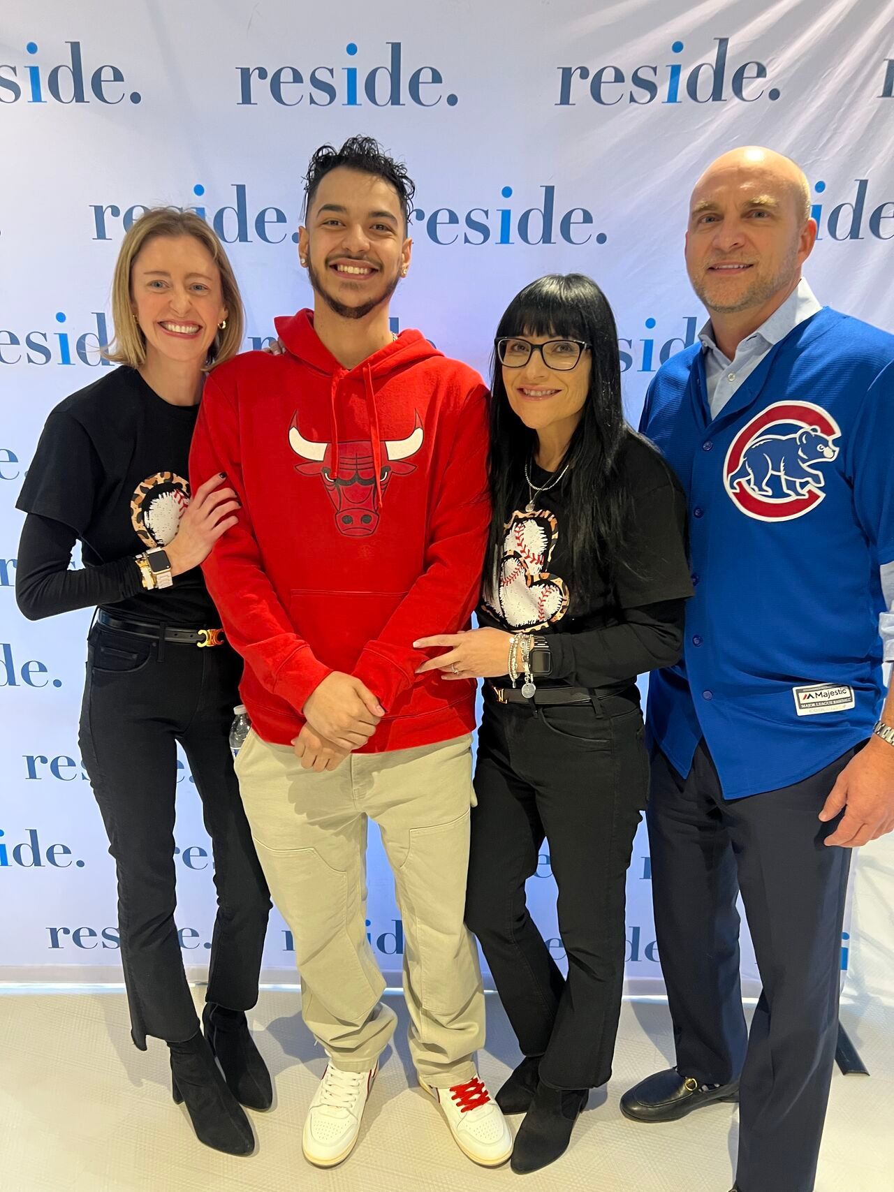 Four people smiling at an event, standing in front of a backdrop with red and blue logos.