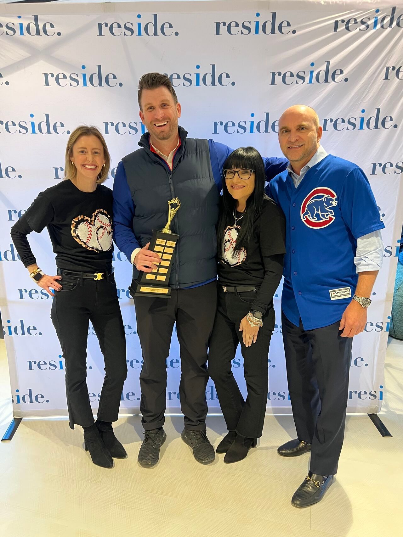 Four people posing with a trophy in front of a “reside” backdrop, smiling at an event