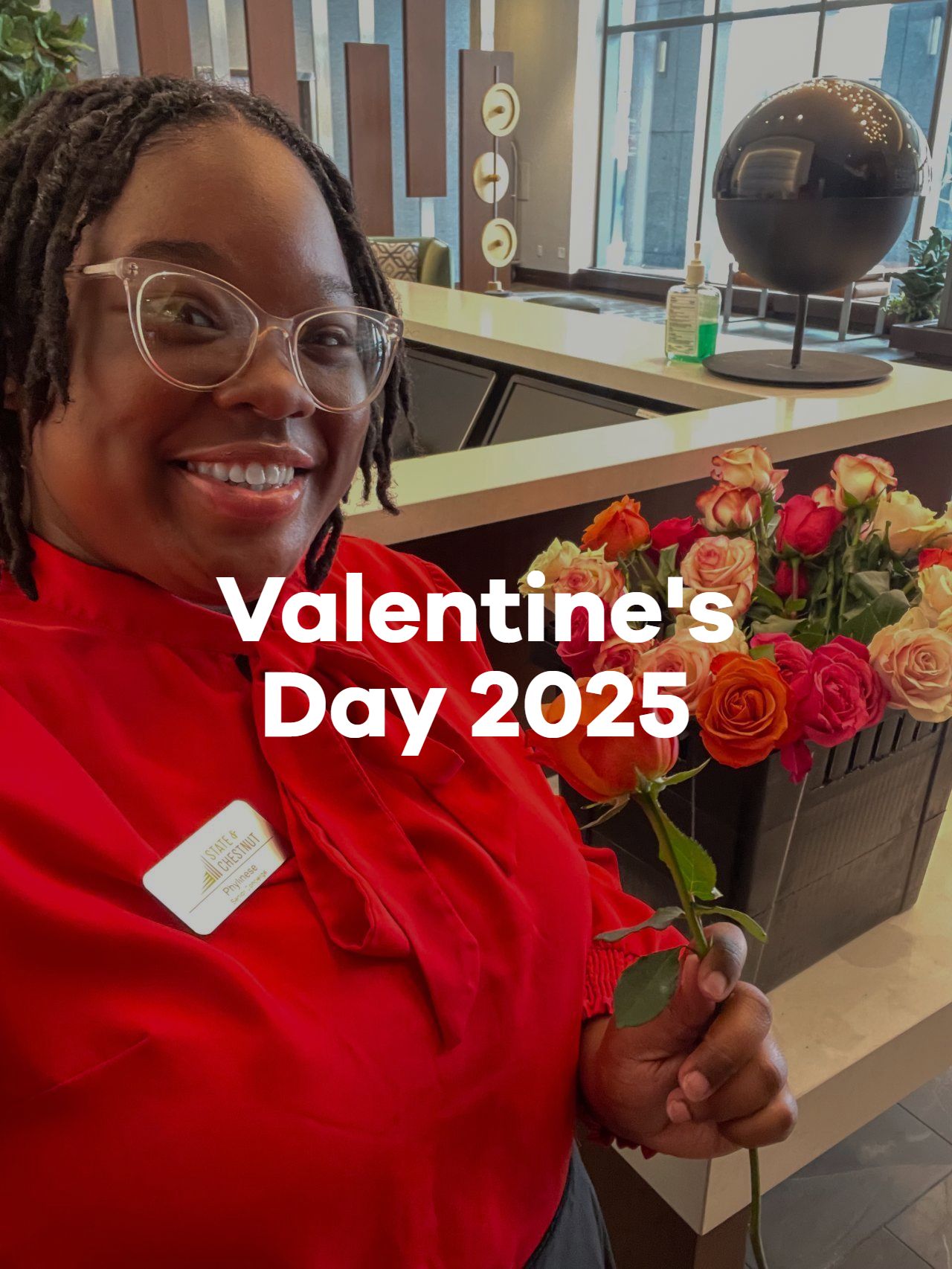 Smiling person in red holding roses with “Valentine’s Day 2025” text in a lobby