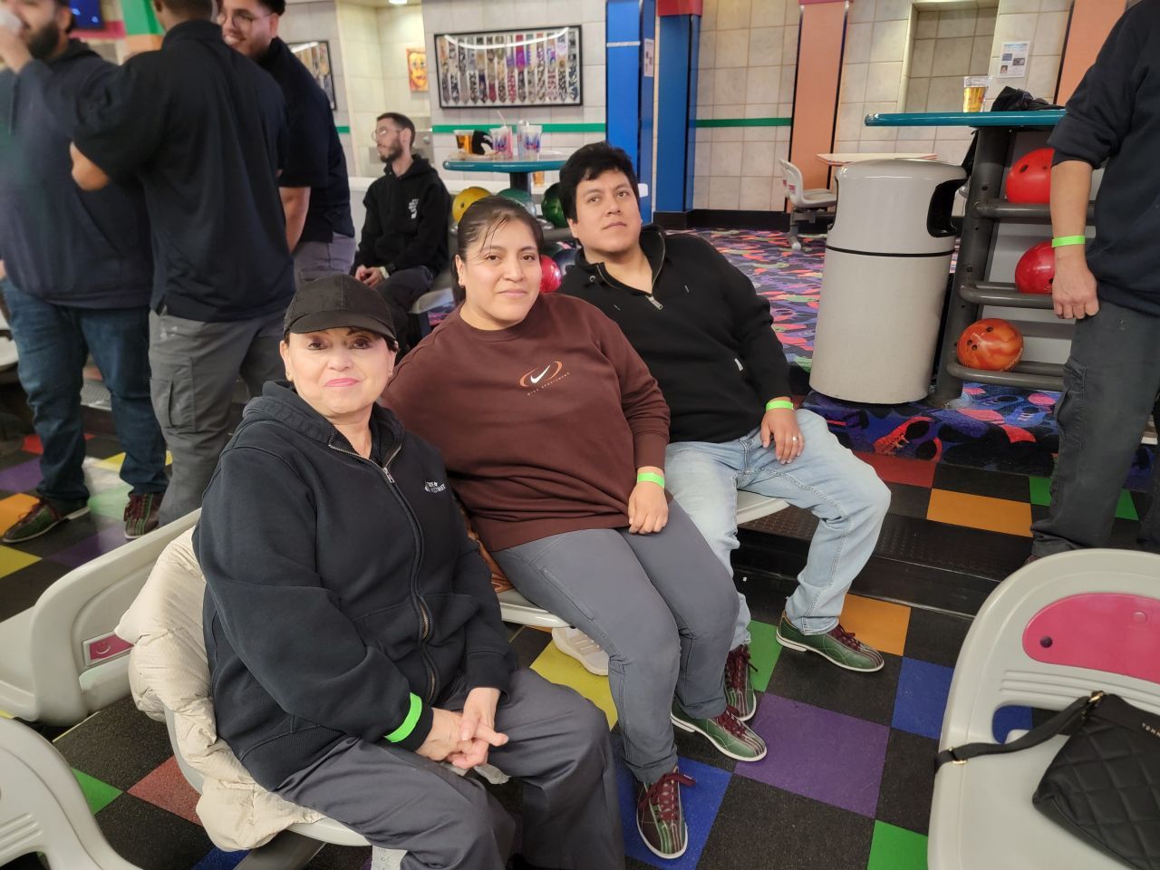 Three people sitting on benches in a colorful indoor space, looking at the camera.
